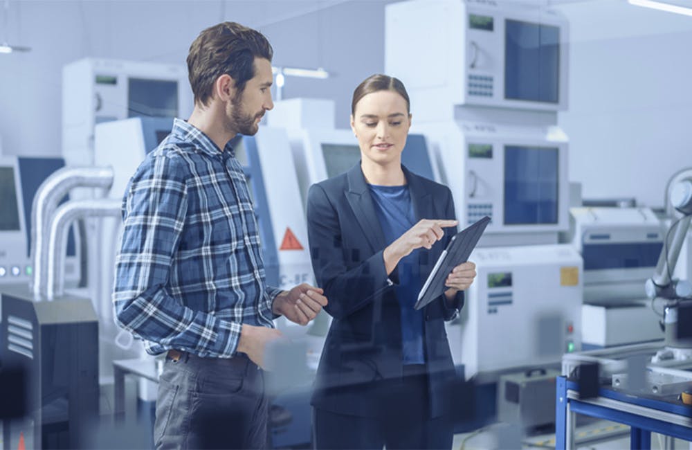 Modern Factory: Female Project Manager and Male Engineer Standing, Talking, Using Digital Tablet for Programming and Monitoring Assembly Line.