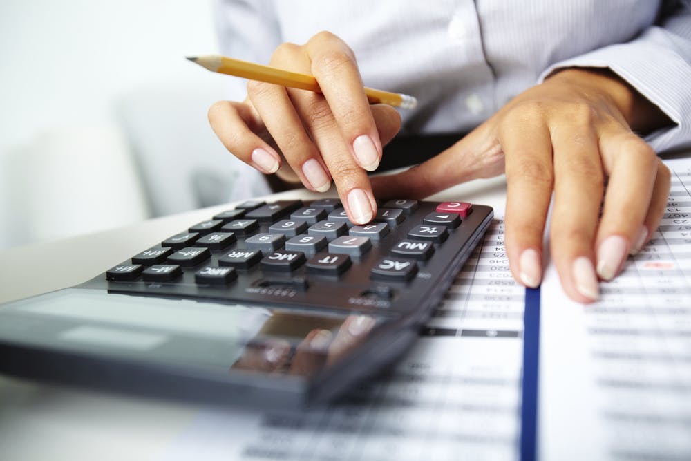 image of photo of hands holding pencil and pressing calculator buttons over documents