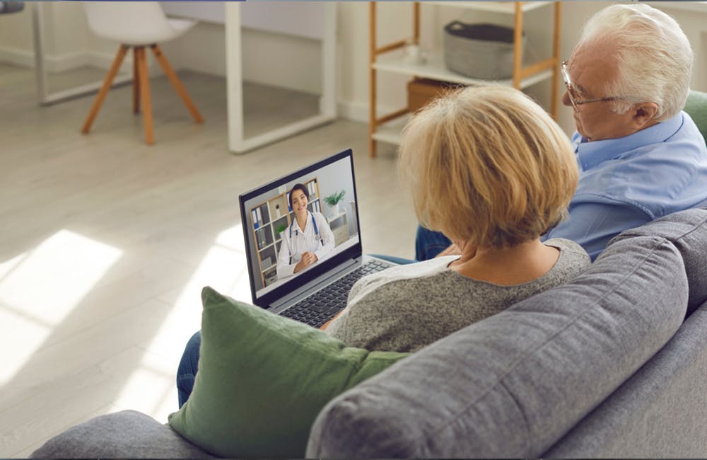 image of Couple of senior patients sitting on sofa with laptop, having video call with online doctor and getting professional health consultation