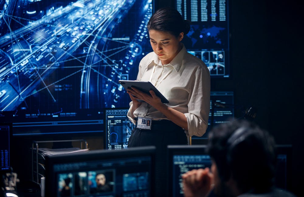 An FBI special agent uses a digital tablet to check the information she receives. The girl is in the CIA office, behind her are huge digital panels that display information from satellites in real time.