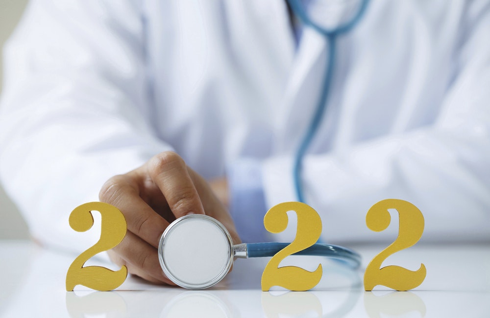 Doctor holding stethoscope near gold wooden number 2022 on desk. Idea for new trend in medicine treatment and diagnosis.