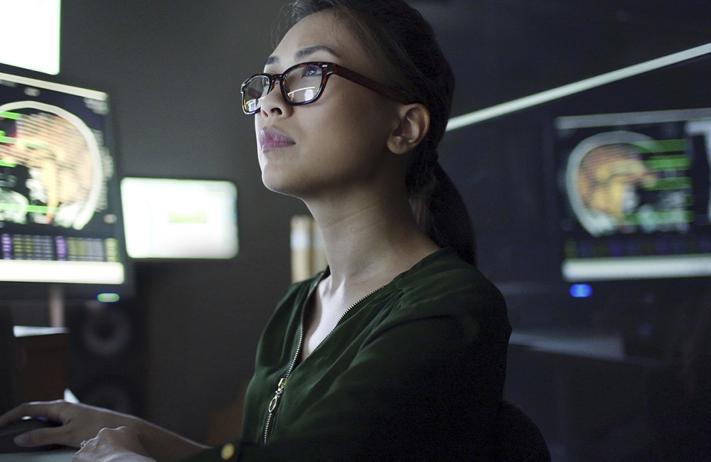 woman works on computer with brain scans on screens behind her