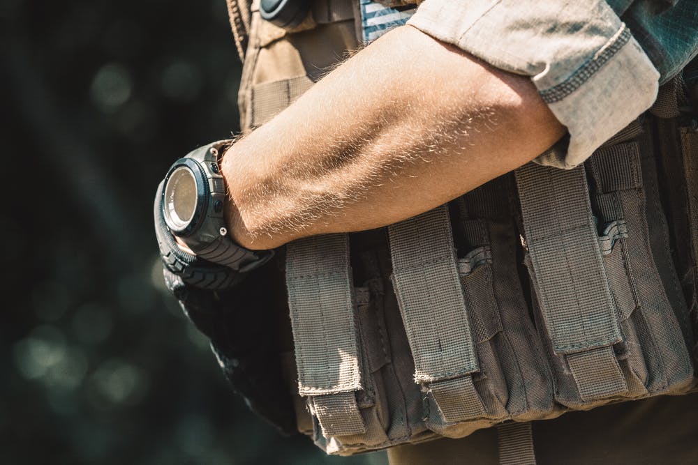 image of Male soldier wearing a bulletproof vest and a shirt with short sleeves. On hand watches.