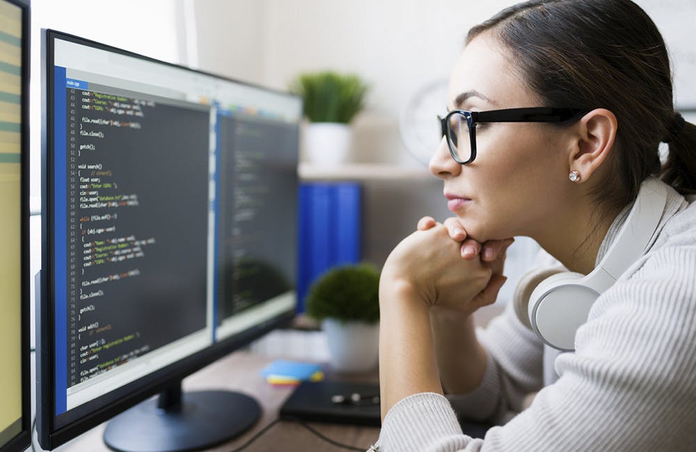 Profile of a freelancer wearing glasses and reading the coding software on the computer. Focused programmer checking the app code