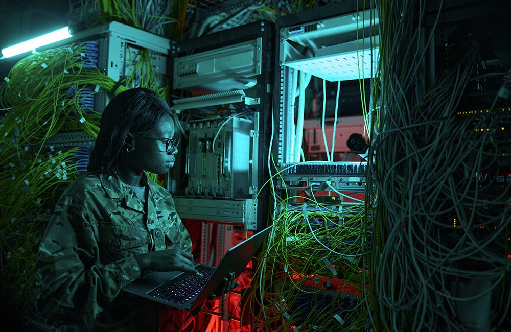 conceptual image of woman wearing military uniform inspecting server representing how ai and automation are vital to navy's cyber readiness