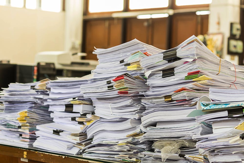 image of five large stacks of paper files sitting on table.