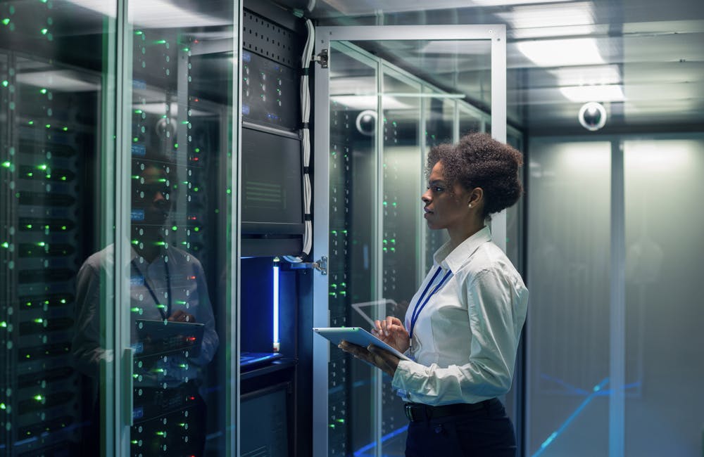 image of shot of female technician working on a tablet in a data center full of rack servers running diagnostics and maintenance on the system