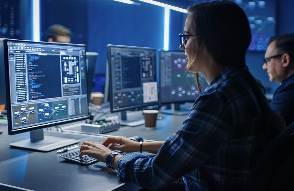 image of female IT Programer Working on Desktop Computer in Data Center System Control Room representing software supply chain security at CFPB, DOE