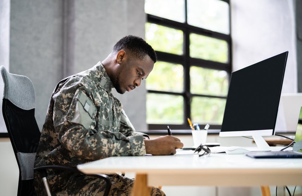 image of veteran taking notes in front of computer intended to represent how the department of veterans affairs is overseeing digitalization of its education support and scholarship benefits.