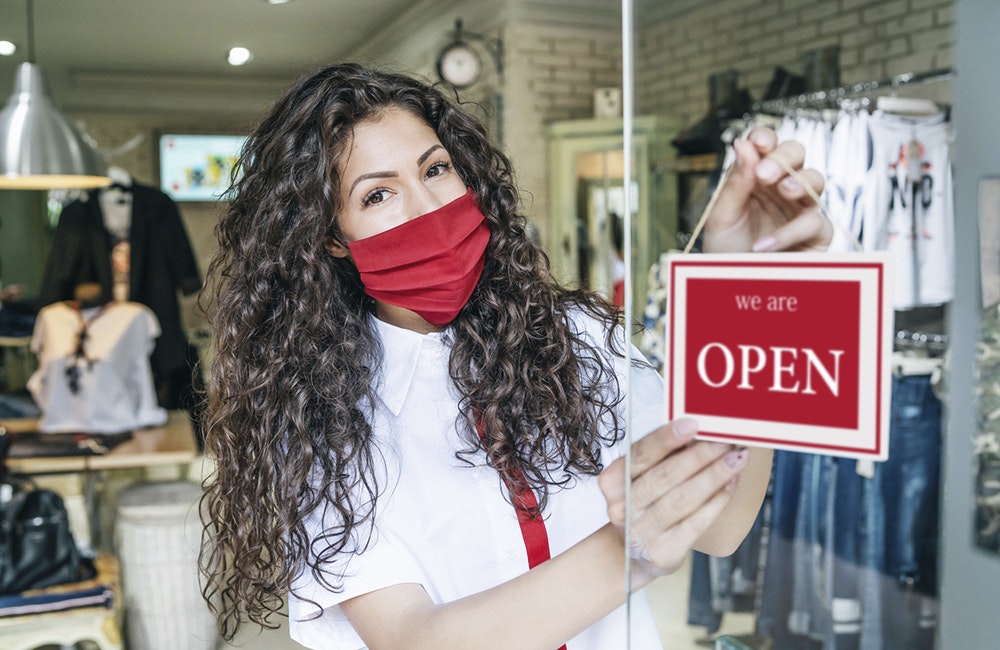 Happy business owner hanging an open sign during COVID-19