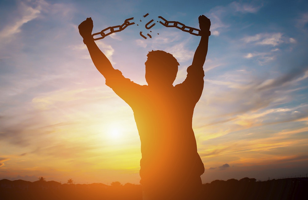 Silhouette image of a businessman with broken chains in sunset