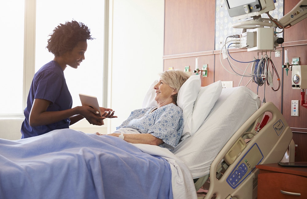 Hospital Nurse With Digital Tablet Talks To Senior Patient