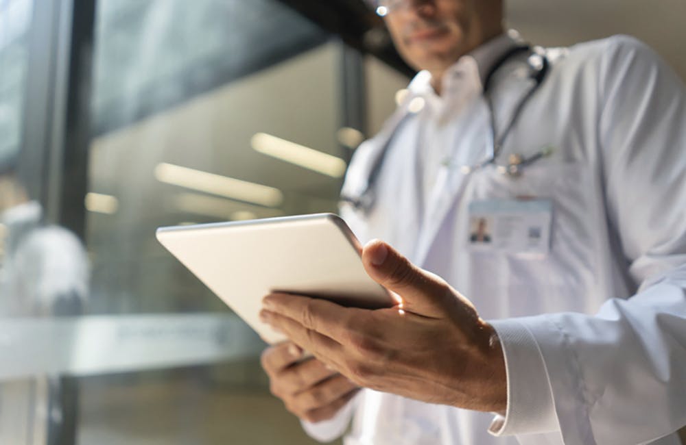 Male doctor at the hospital looking at a medical chart on tablet - Low angle view