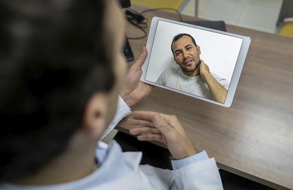 Patient on a video call with a doctor through a tablet computer and complaining about neck pain - healthcare concepts