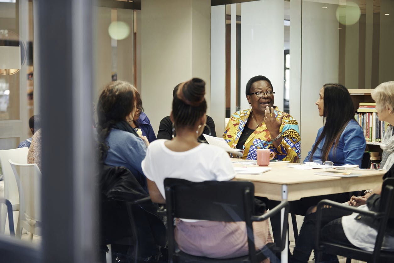 hot of a group of confident women seated around a table talking to each other during a meeting inside of a community centre