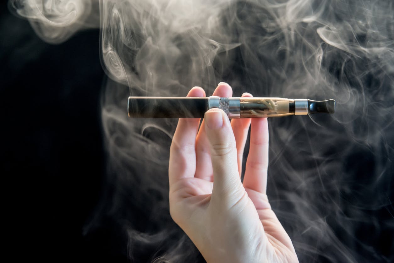 Photo of woman Hand holding an electronic cigarette over a dark background with smoke