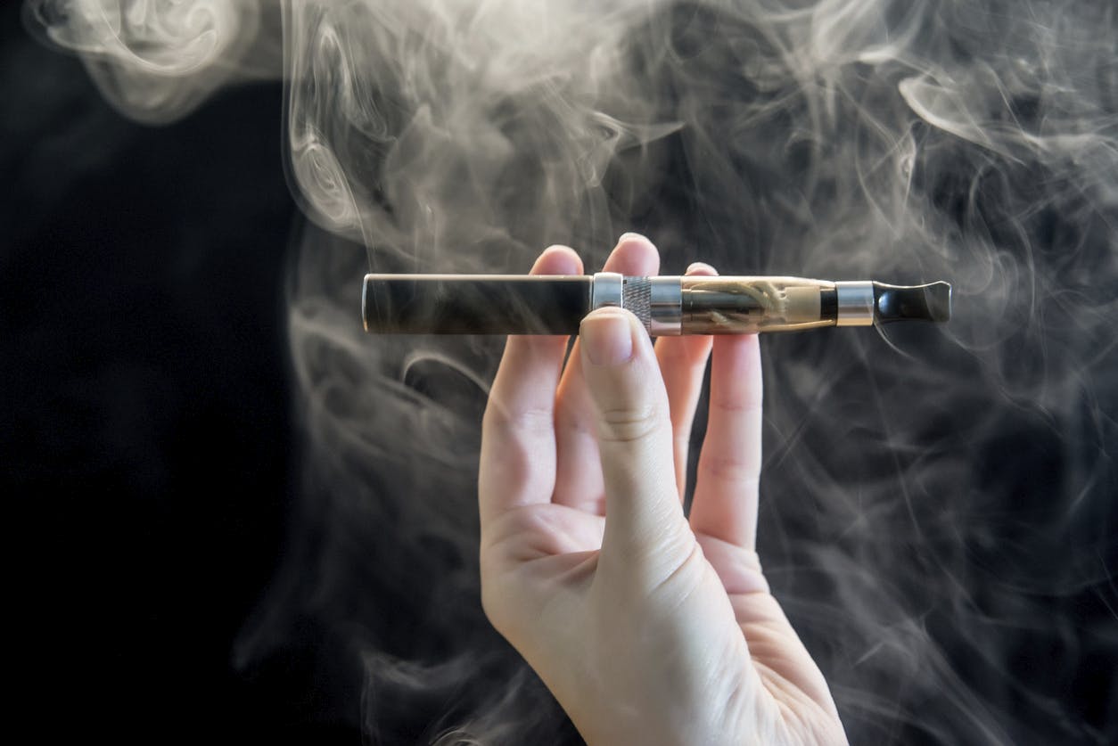 Photo of woman Hand holding an electronic cigarette over a dark background with smoke