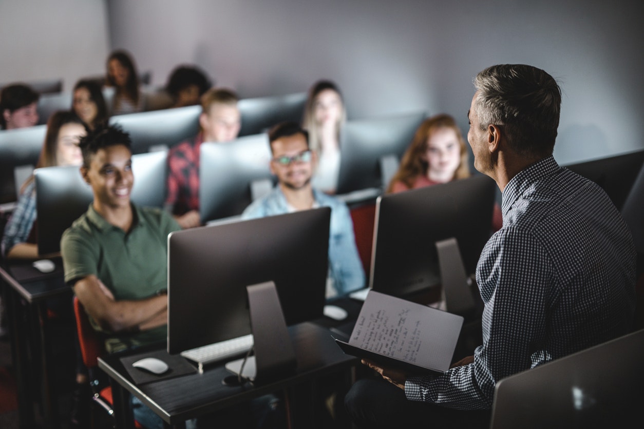 Male teacher talking to large group of students on a class at computer lab.